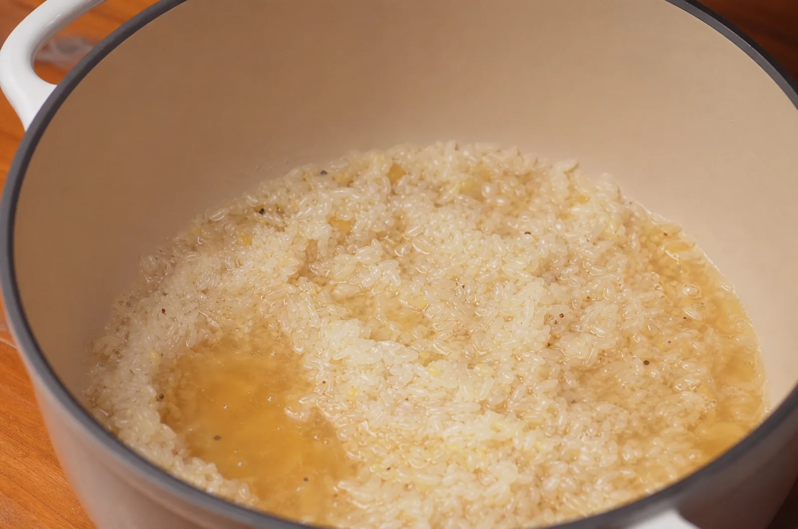 Fragrant rice simmering in chicken broth in a white cooking pot